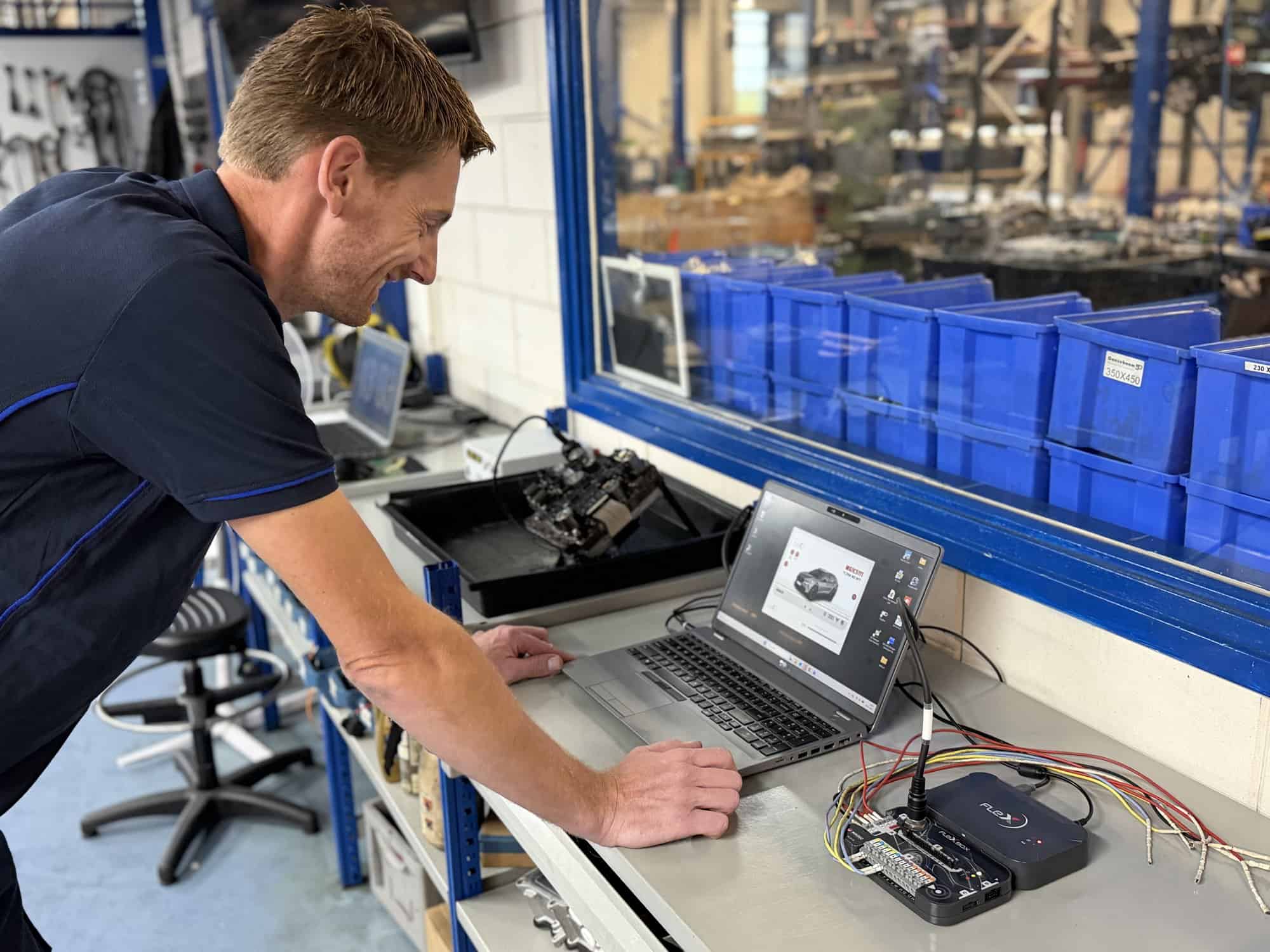 A Ganzeboom employee looking up a transmission part on the laptop in the workshop, with stock bins and a stripped component on the bench.